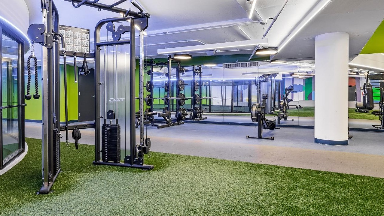 Dynamic gym space with artificial turf flooring, strength training equipment, and bright lighting at River City Apartments in Chicago