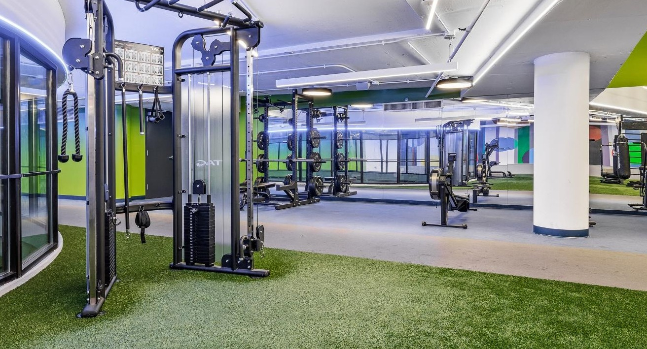 Dynamic gym space with artificial turf flooring, strength training equipment, and bright lighting at River City Apartments in Chicago