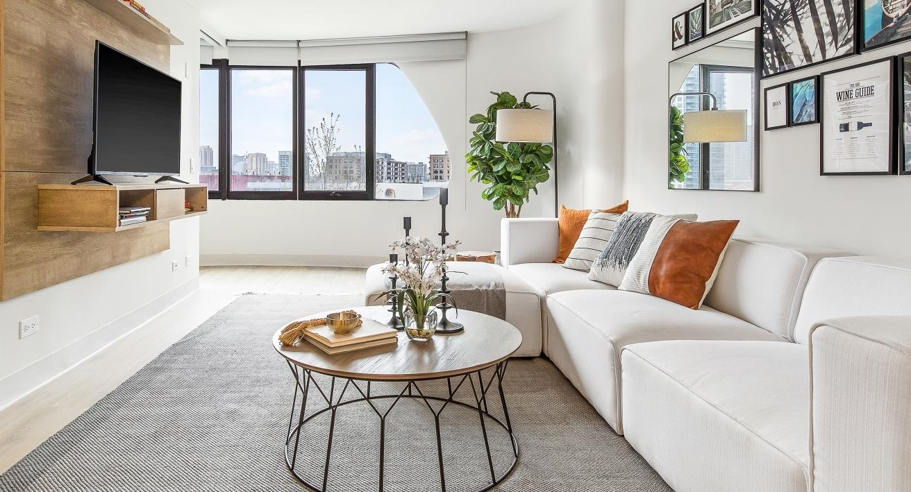 Bright, modern living room with a white sectional sofa, stylish decor, and large windows at River City Apartments in Chicago