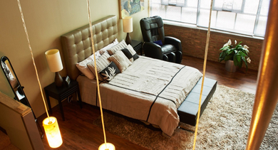 A cozy loft bedroom with a large bed, plush rug, an accent chair, and high windows, offering an elevated perspective at River West Lofts in Chicago