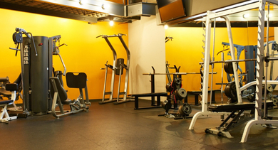 A vibrant fitness center featuring a range of weightlifting and strength training equipment against a bright yellow wall at River West Lofts in Chicago