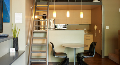 A modern loft kitchen with light cabinetry, stainless steel appliances, a breakfast bar, and stairs leading to a mezzanine level at River West Lofts in Chicago