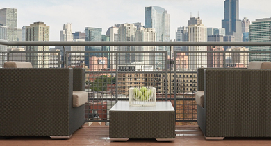 A rooftop seating area with woven armchairs and a coffee table, offering a magnificent view of the Chicago city skyline at River West Lofts