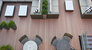 An inviting rooftop lounge area with extensive sectional sofas, coffee tables, and small dining sets on wooden decking at River West Lofts in Chicago