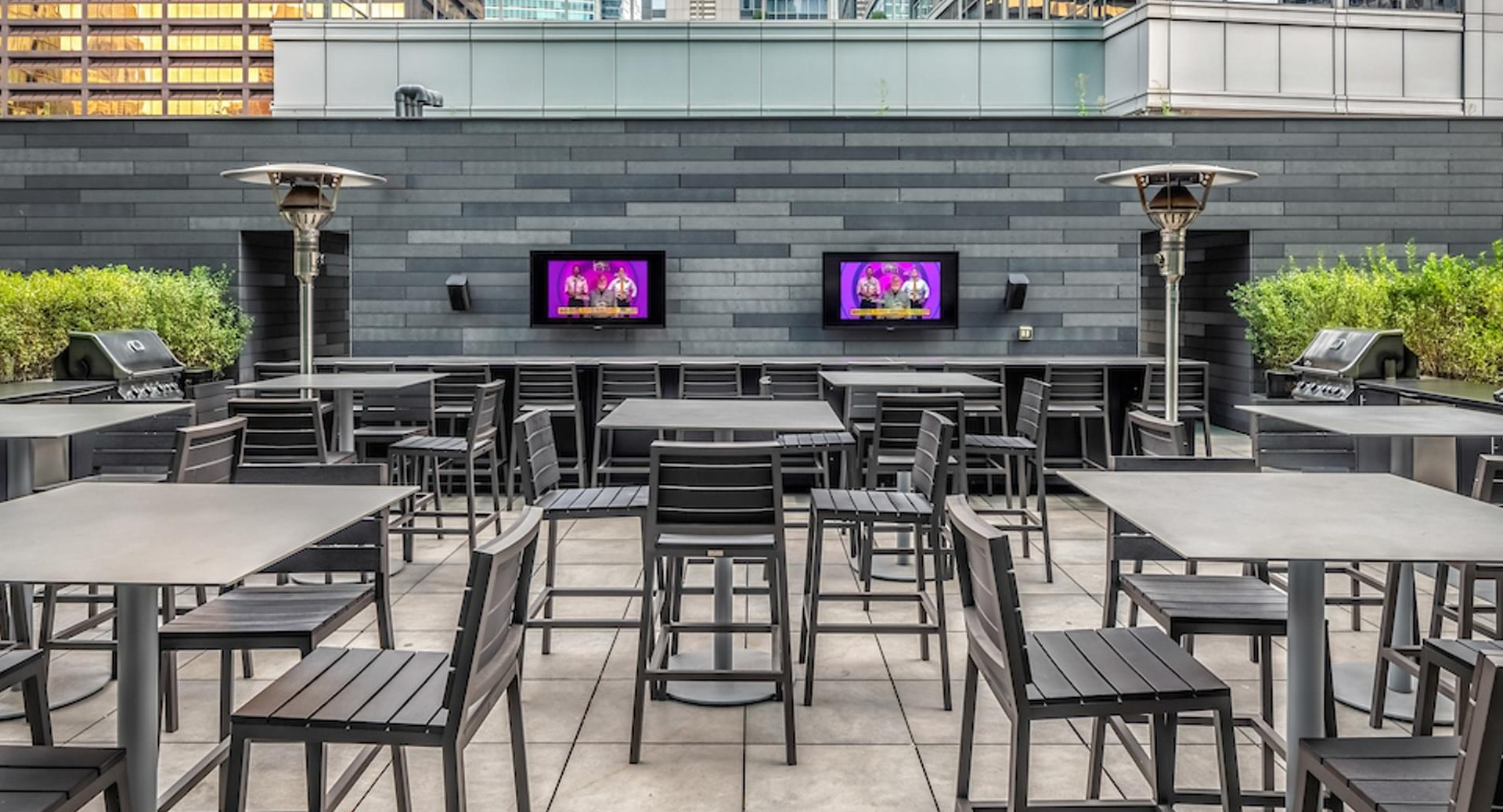 Rooftop grilling lounge with dining tables, TVs, and stainless-steel BBQ stations surrounded by city views at Optima Signature Chicago