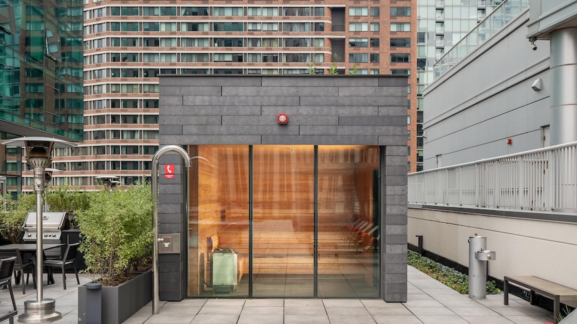 Rooftop sauna with glass walls, surrounded by lounge chairs, BBQ grills, and city views at Optima Signature apartments in Chicago