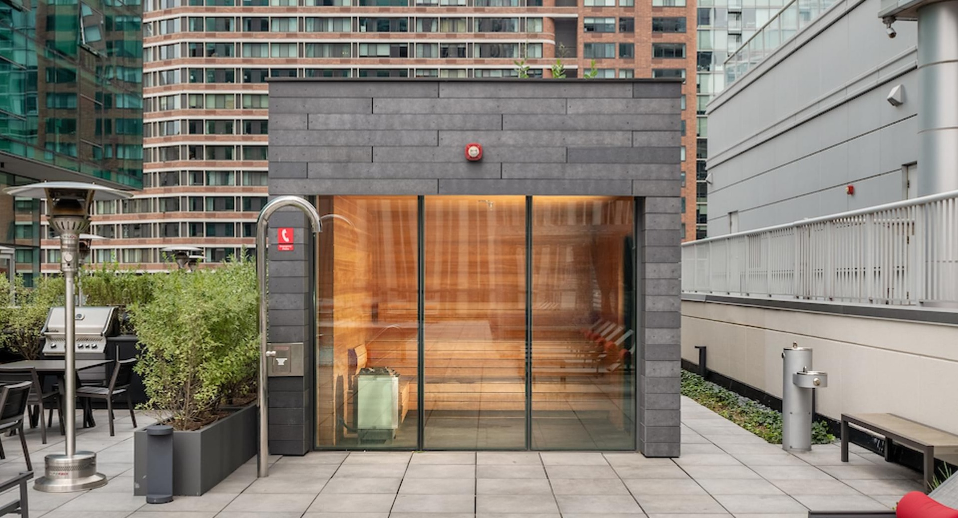 Rooftop sauna with glass walls, surrounded by lounge chairs, BBQ grills, and city views at Optima Signature apartments in Chicago