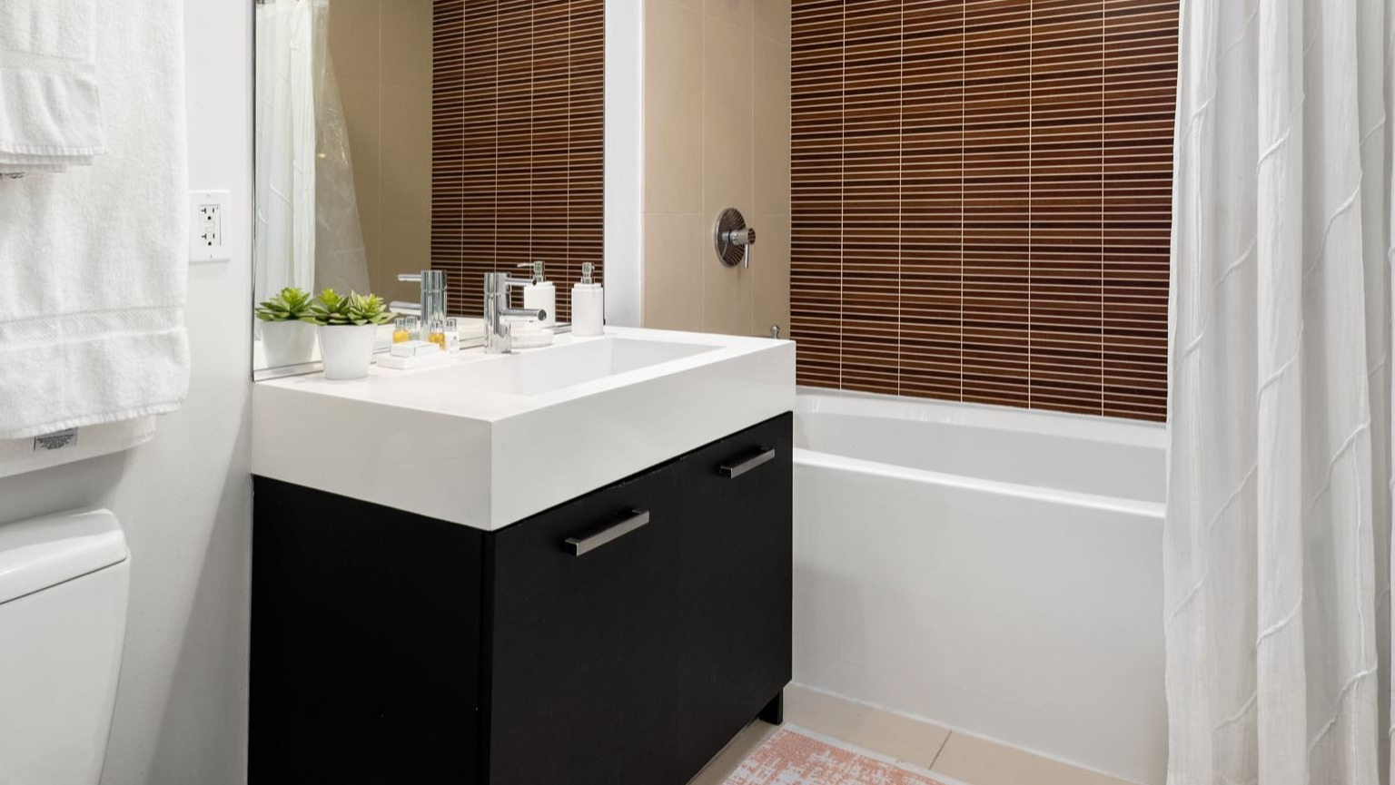 Contemporary bathroom with a modern vanity, spacious sink, and a tiled shower with a white curtain at Roosevelt Collection Lofts