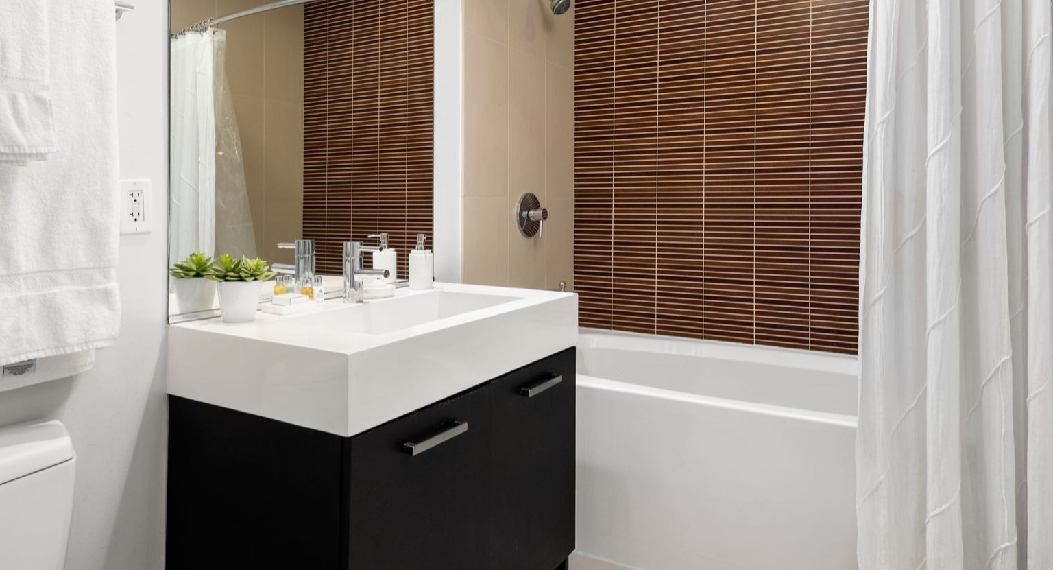 Contemporary bathroom with a modern vanity, spacious sink, and a tiled shower with a white curtain at Roosevelt Collection Lofts