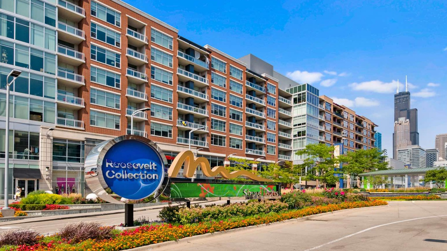 Exterior view of Roosevelt Collection Lofts with a prominent sign, lush landscaping, and a bustling urban setting