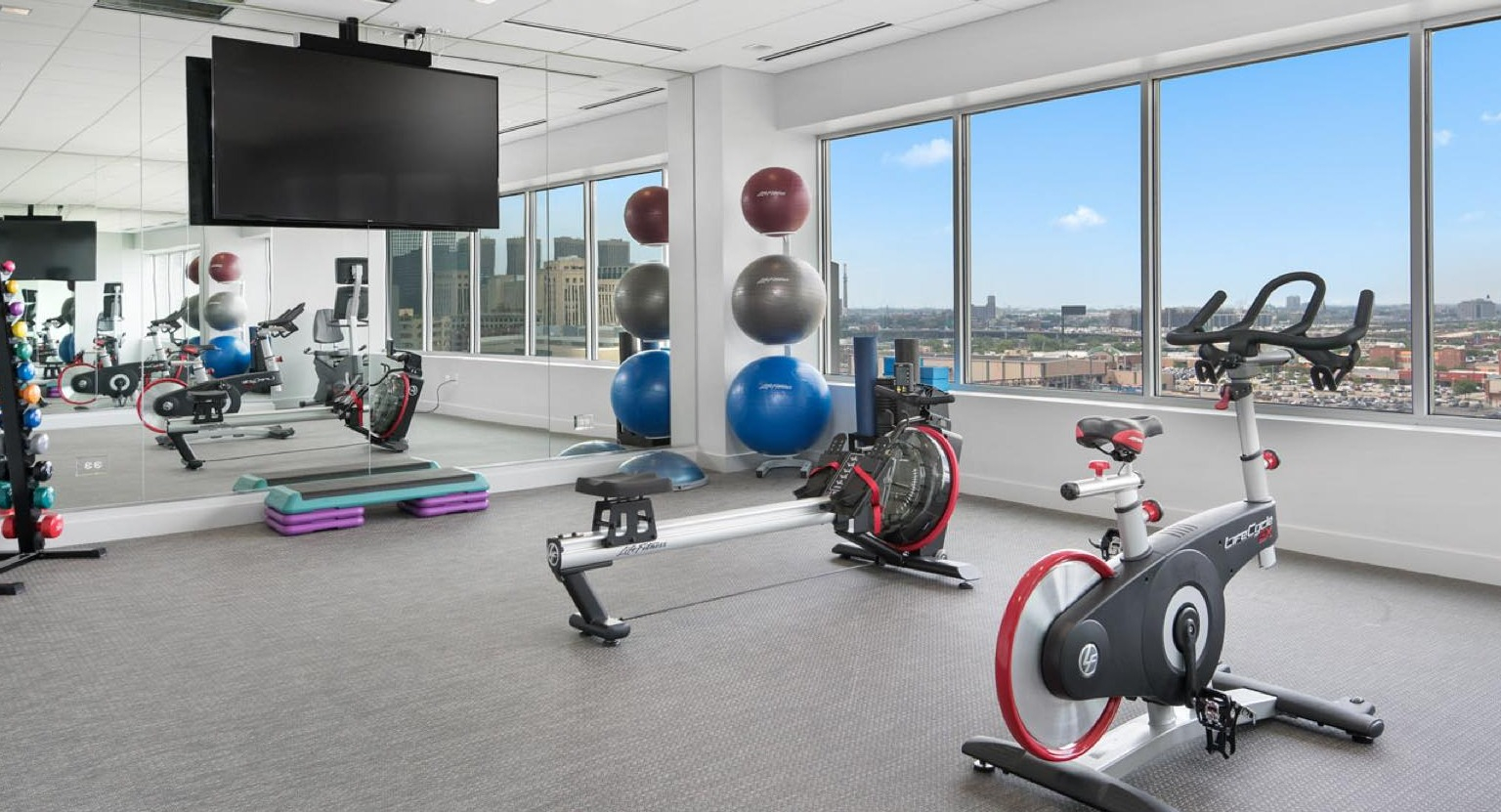 Bright fitness studio with various cardio machines, exercise balls, and large windows overlooking the city at Roosevelt Collection Lofts