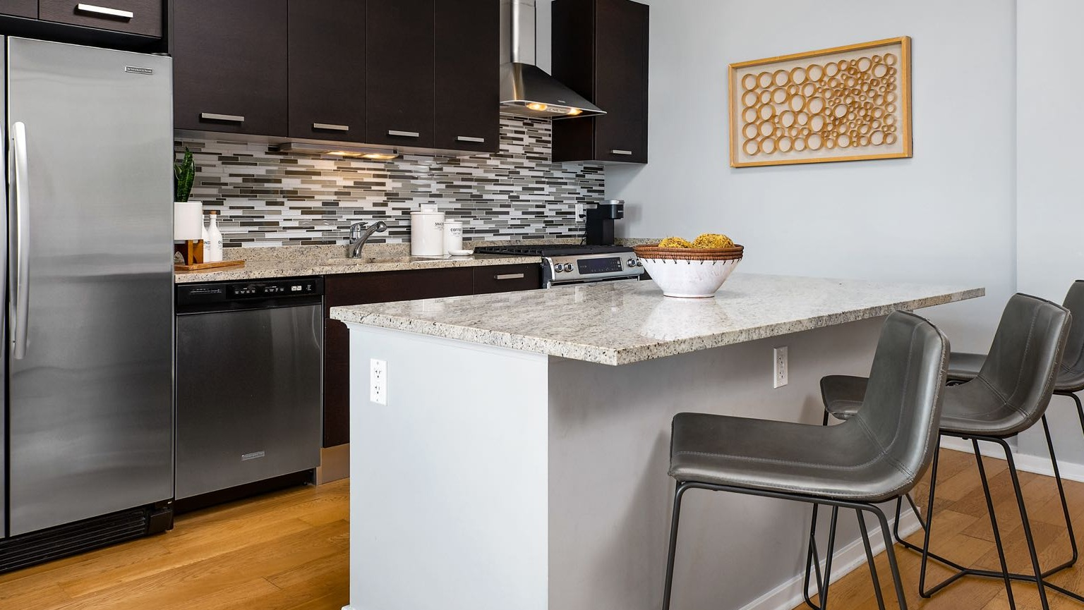 Modern kitchen at Roosevelt Collection Lofts in Chicago, featuring dark wood cabinets, stainless steel appliances, and a granite island with seating