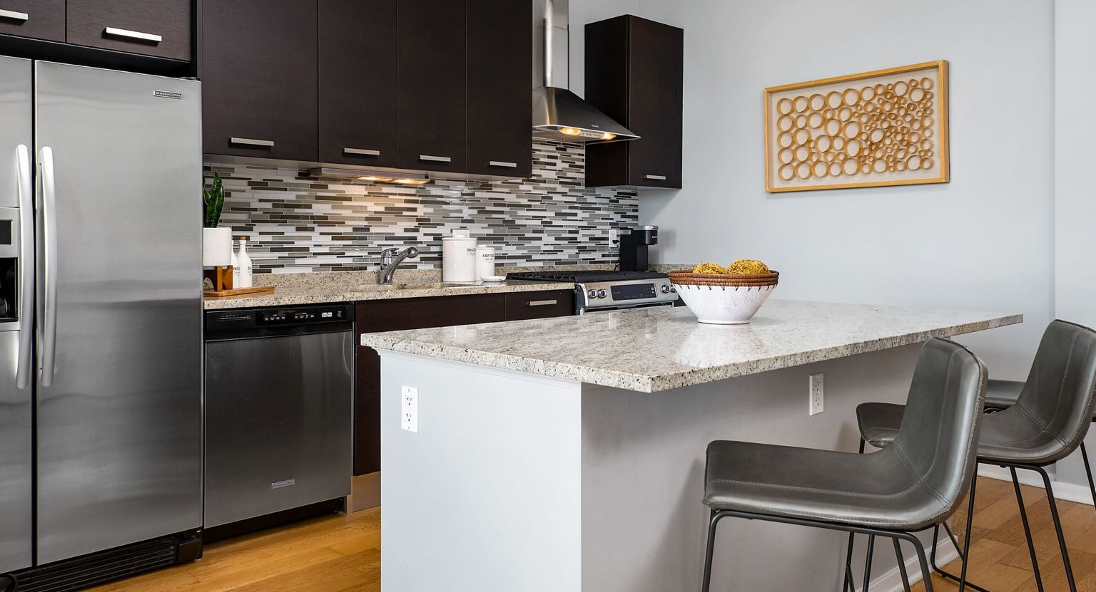 Modern kitchen at Roosevelt Collection Lofts in Chicago, featuring dark wood cabinets, stainless steel appliances, and a granite island with seating