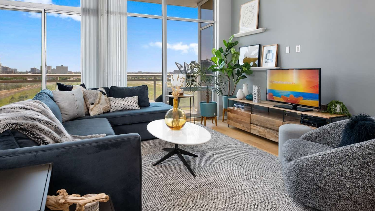 Inviting living room at Roosevelt Collection Lofts in Chicago, featuring a sunny yellow sofa, stylish rug, and expansive windows with city views