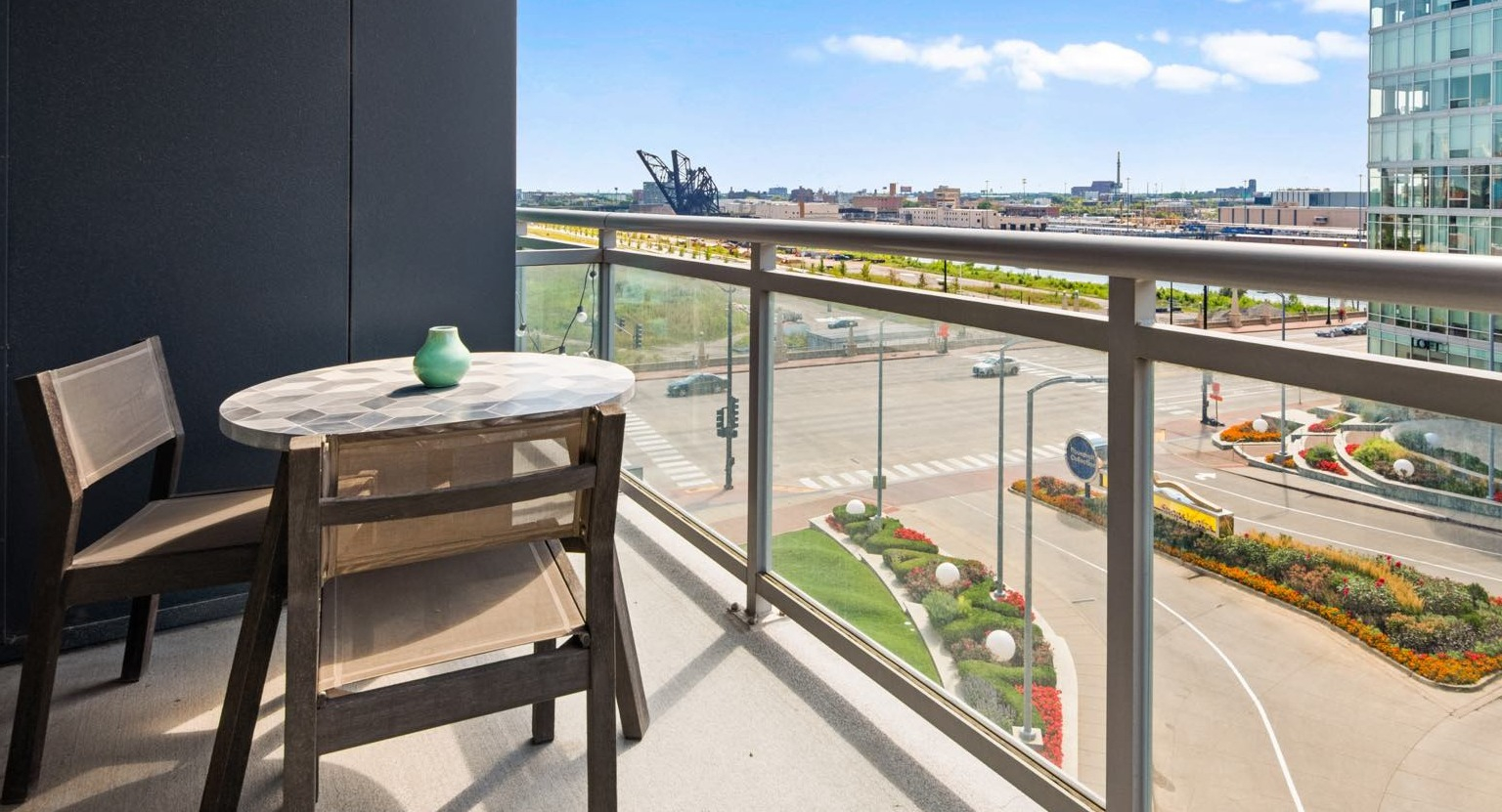 Private apartment balcony with a small table and chairs, offering views of the city street and landscaped areas at Roosevelt Collection Lofts 