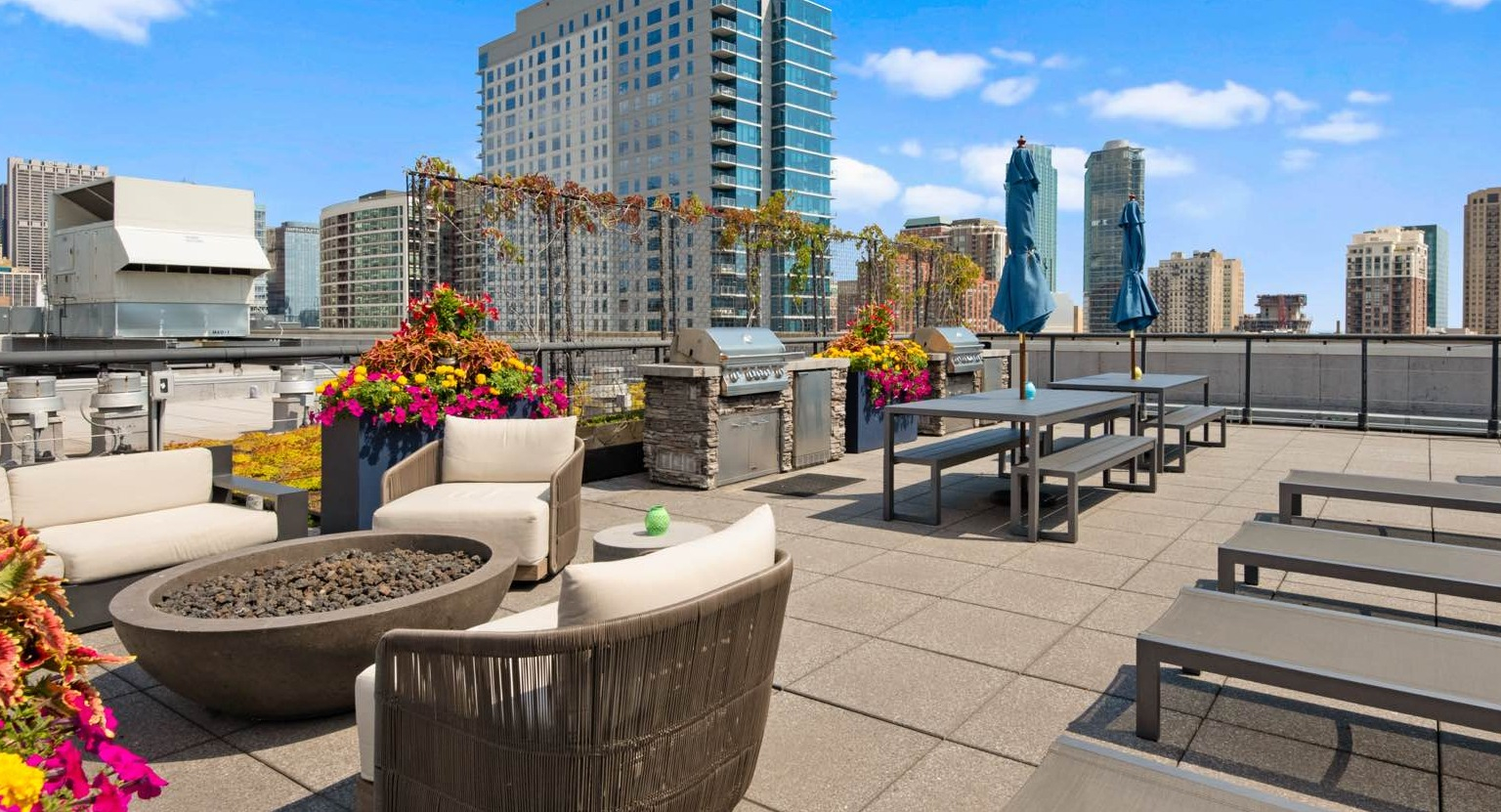 Spacious rooftop lounge area with a cozy fire pit, comfortable seating, sun loungers, and city views at Roosevelt Collection Lofts