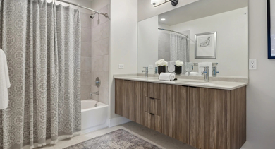Spacious apartment bathroom at Sage West Loop Apartments in Chicago, featuring a double vanity, large mirror, and a bathtub with shower