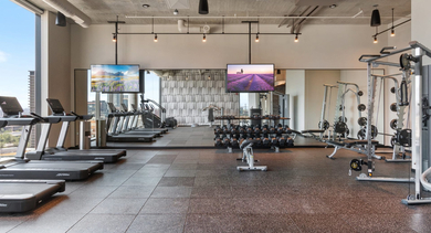 State-of-the-art gym at Sage West Loop Apartments in Chicago, featuring cardio machines, weight racks, and large windows with city views