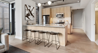 Elegant apartment kitchen at Sage West Loop Apartments in Chicago, featuring a large island with bar stools, and modern light wood cabinets