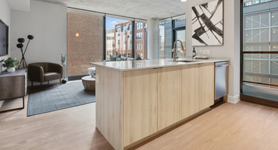 Contemporary kitchen and living area at Sage West Loop Apartments in Chicago, featuring light wood cabinets, an island, and an open layout
