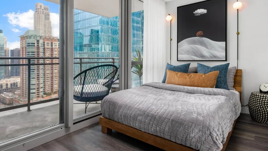 Cozy bedroom at Shoreham and Tides apartments in Chicago with floor-to-ceiling glass, private balcony seating, and modern bed styling