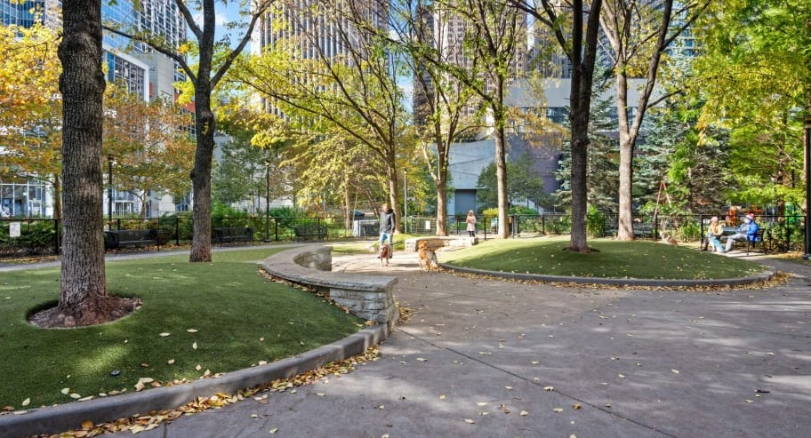 Spacious dog park with walking paths, green turf, and shaded trees for residents and pets at Shoreham and Tides apartments in Chicago
