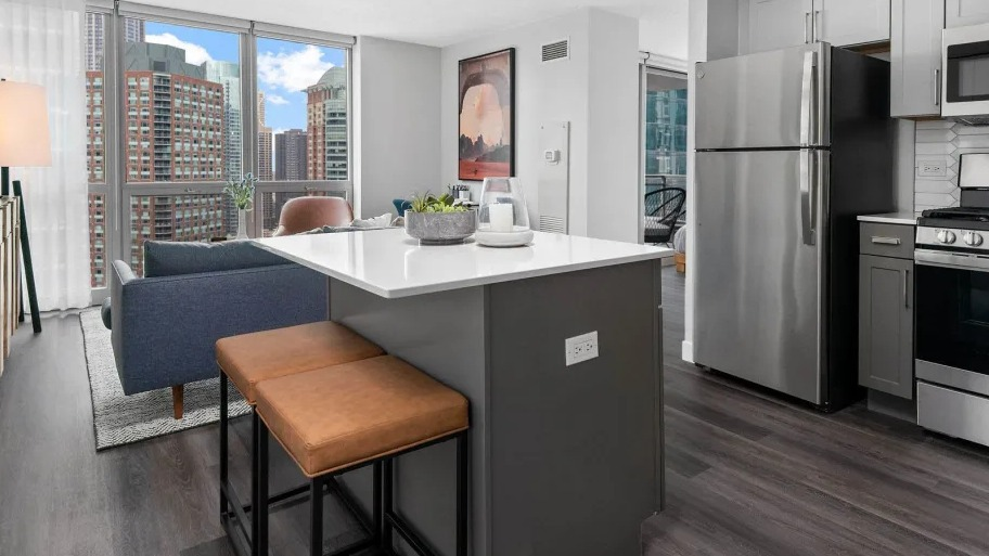 Open kitchen with island seating at Shoreham and Tides apartments in Chicago, stainless appliances, and bright city views through large windows