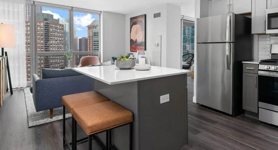 Open kitchen with island seating at Shoreham and Tides apartments in Chicago, stainless appliances, and bright city views through large windows