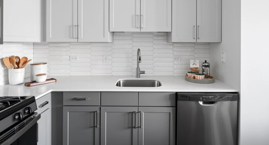 Bright kitchen at Shoreham and Tides apartments in Chicago featuring white tile backsplash, sleek faucet, and gray cabinetry with ample storage