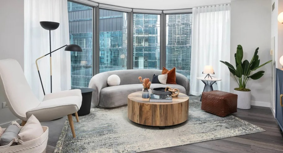 Modern living room at Shoreham and Tides apartments in Chicago featuring curved floor-to-ceiling windows, a round coffee table, and stylish seating