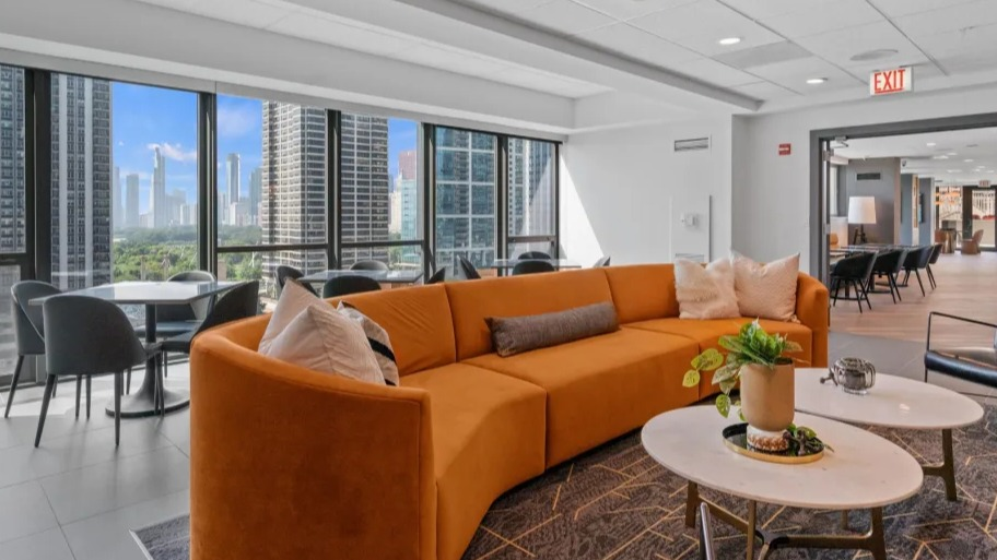 Bright resident lounge at Shoreham and Tides in Chicago with curved sofa, café tables, and sweeping skyline views through floor-to-ceiling windows