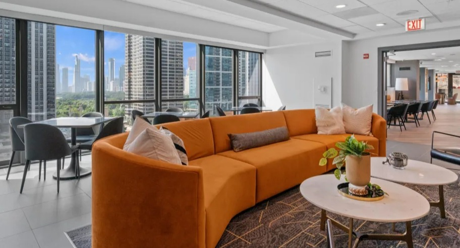 Bright resident lounge at Shoreham and Tides in Chicago with curved sofa, café tables, and sweeping skyline views through floor-to-ceiling windows