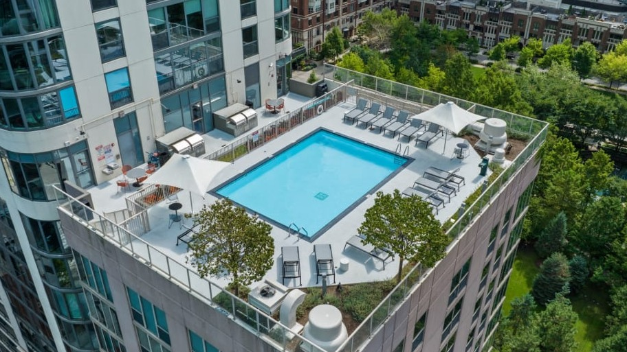 Rooftop pool and sun deck at Shoreham and Tides apartments in Chicago featuring lounge chairs, greenery, and scenic city and lake views