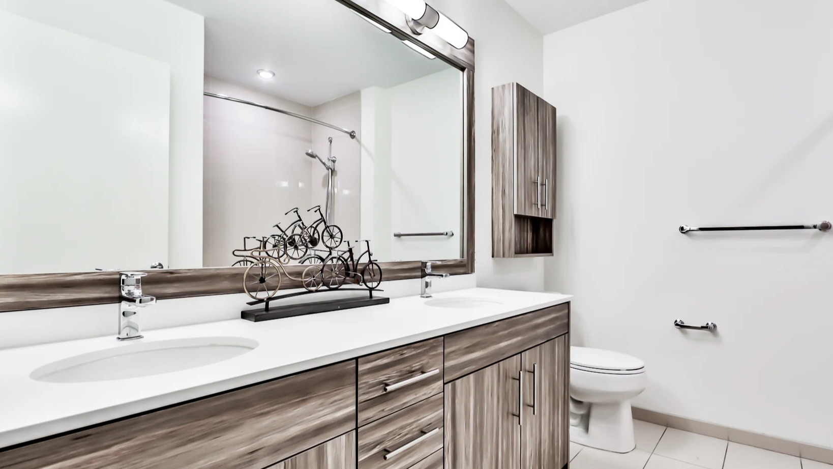 Modern bathroom at Sienna in Chicago, featuring a double vanity with ample storage, a large mirror, and clean white tiling