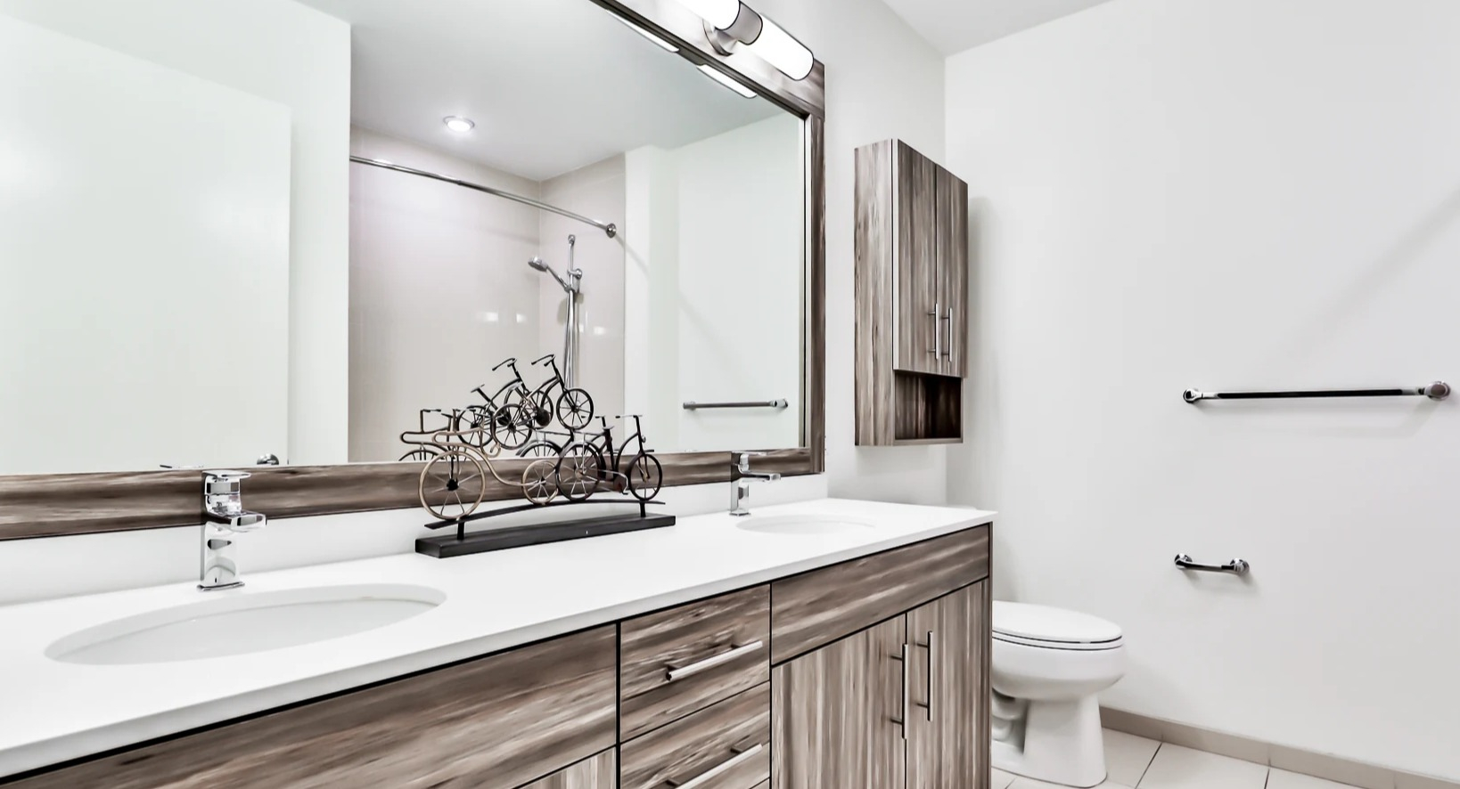 Modern bathroom at Sienna in Chicago, featuring a double vanity with ample storage, a large mirror, and clean white tiling