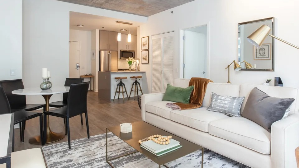 Modern open-concept living, dining, and kitchen area at Sienna in Chicago, featuring a white sofa, round dining table, and bar seating