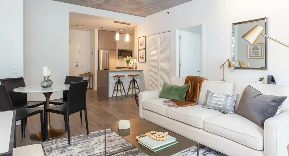 Modern open-concept living, dining, and kitchen area at Sienna in Chicago, featuring a white sofa, round dining table, and bar seating