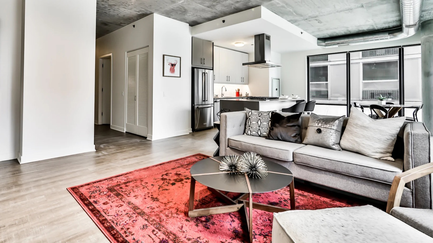 Modern living area and kitchen at Sienna in Chicago, featuring a comfortable gray sofa, vibrant rug, and open access to a contemporary kitchen