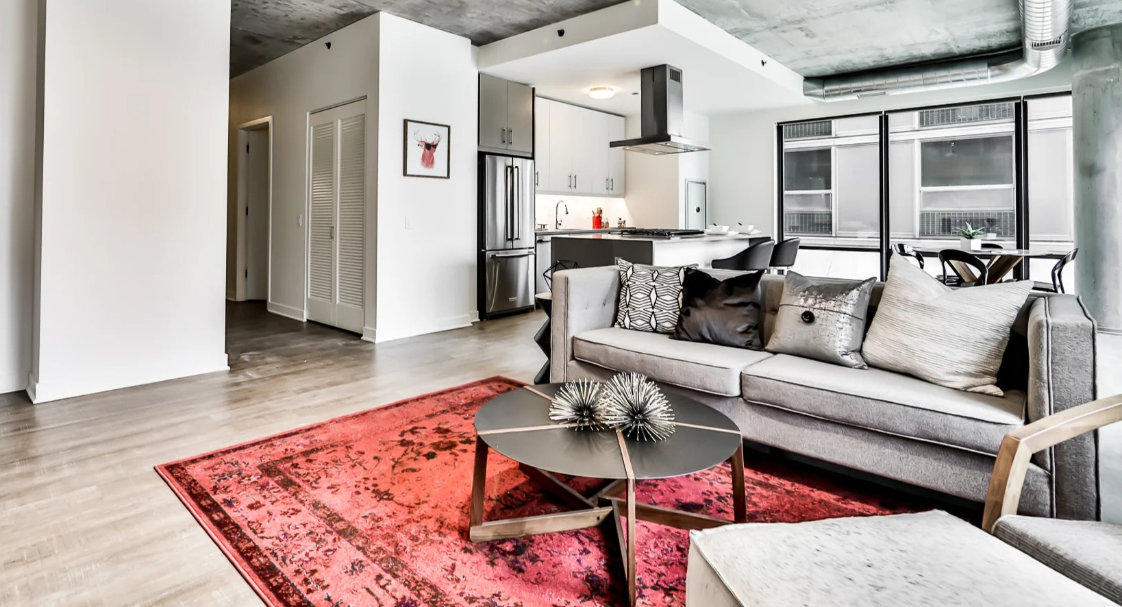 Modern living area and kitchen at Sienna in Chicago, featuring a comfortable gray sofa, vibrant rug, and open access to a contemporary kitchen