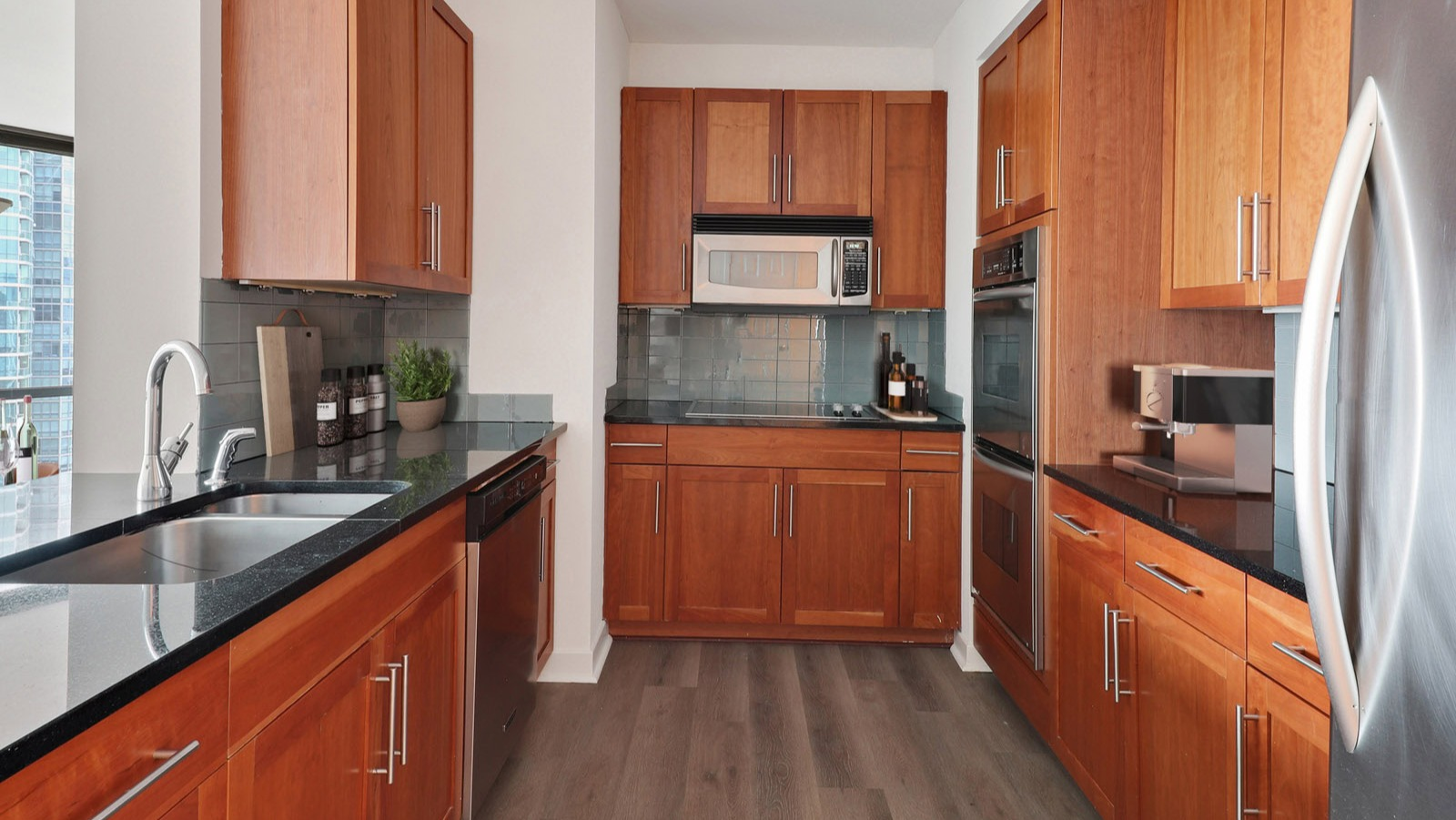 Gourmet kitchen featuring warm wood cabinetry, dark countertops, stainless steel appliances, and an open layout at SKY55 apartments in Chicago