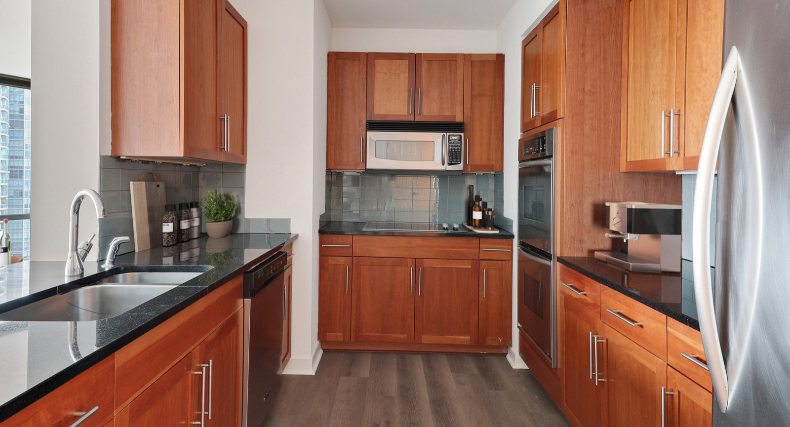 Gourmet kitchen featuring warm wood cabinetry, dark countertops, stainless steel appliances, and an open layout at SKY55 apartments in Chicago