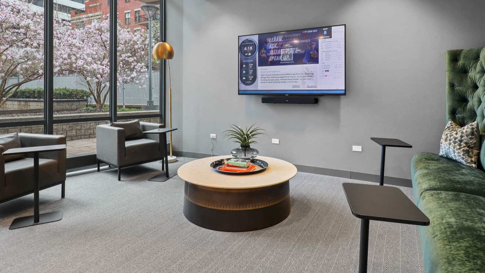 Cozy resident lounge with a plush green sofa, armchairs, and views of a lush outdoor garden area at SKY55 apartments in Chicago