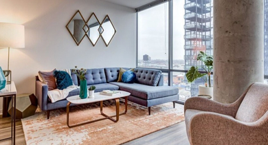 A cozy living room at SoNo East Apartments in Chicago, featuring a comfortable L-shaped sofa and large windows with city views