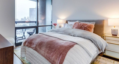 A modern bedroom at SoNo East Apartments in Chicago, boasting a large window and a comfortable bed with soft linens
