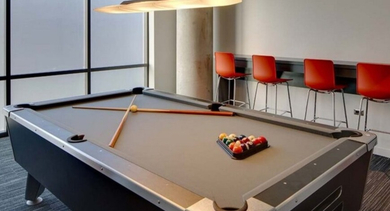 Stylish game room with a billiards table, modern pendant lighting, and bright red bar stools at SoNo East Apartments in Chicago