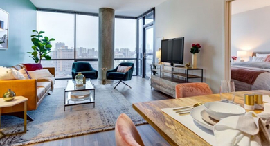 Bright open-concept living and dining area with colorful furniture, city views, and an adjoining bedroom at SoNo East Apartments in Chicago