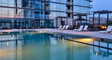 Elegant rooftop pool area at dusk with illuminated water, lounge chairs, and a cozy fire pit at SoNo East Apartments in Chicago
