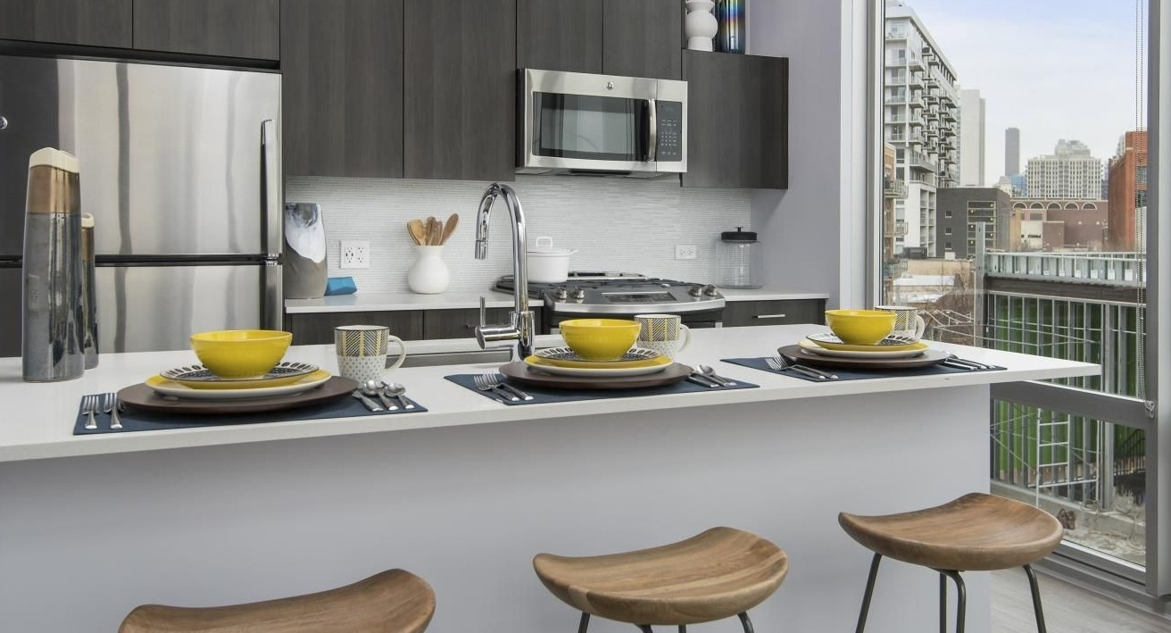 A modern kitchen at Spoke Apartments in Chicago, offering great city views from large windows and counter seating