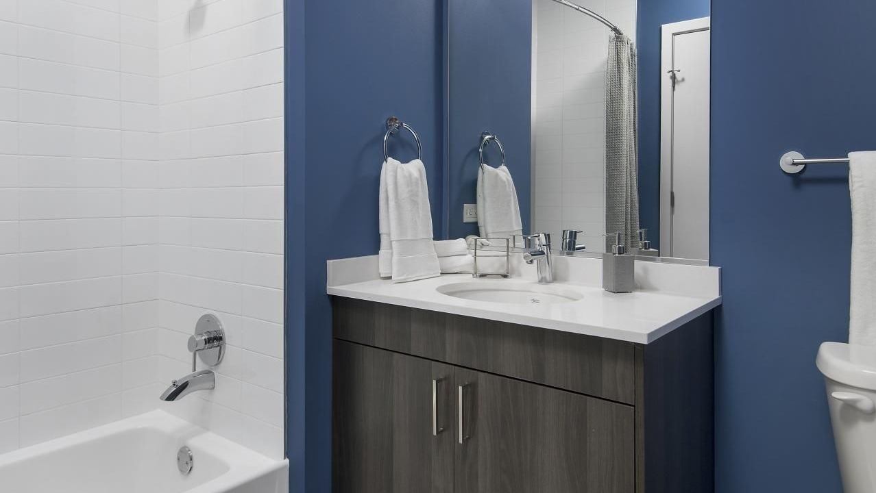 A modern bathroom at Spoke Apartments in Chicago, featuring a dark blue accent wall and contemporary vanity