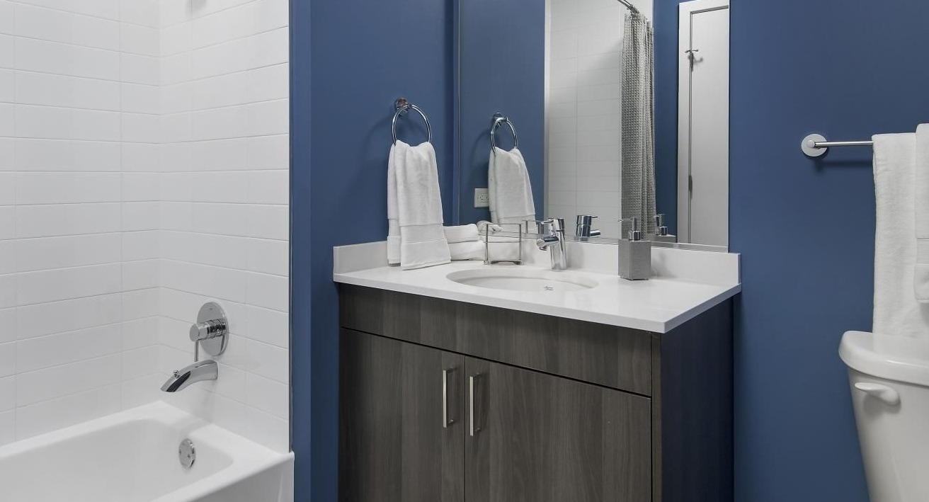 A modern bathroom at Spoke Apartments in Chicago, featuring a dark blue accent wall and contemporary vanity